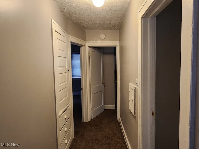 hallway featuring dark colored carpet and a textured ceiling