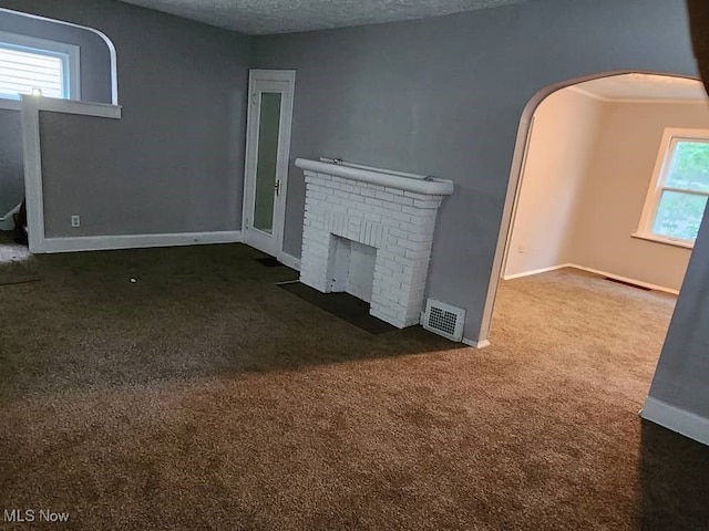 unfurnished living room featuring a fireplace, a textured ceiling, and dark colored carpet