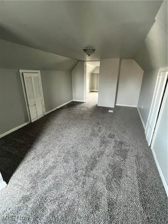 bonus room with vaulted ceiling and dark colored carpet