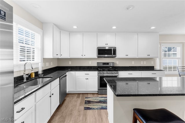 kitchen featuring sink, appliances with stainless steel finishes, white cabinetry, dark stone countertops, and light hardwood / wood-style floors