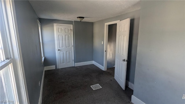 hallway with dark colored carpet and a textured ceiling