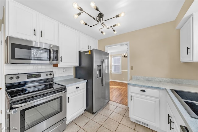 kitchen with an inviting chandelier, light tile patterned flooring, white cabinets, and appliances with stainless steel finishes