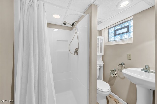 bathroom featuring curtained shower, sink, toilet, a drop ceiling, and tile patterned floors