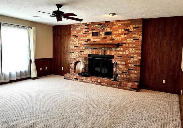 unfurnished living room with light colored carpet, a fireplace, a textured ceiling, and wood walls