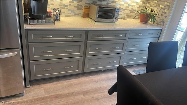 interior space with backsplash, stainless steel fridge, light hardwood / wood-style floors, and gray cabinets