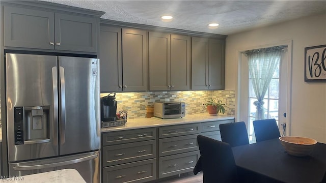 kitchen featuring stainless steel fridge, a toaster, gray cabinets, light countertops, and backsplash