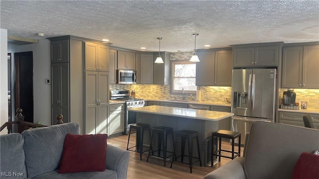 kitchen with appliances with stainless steel finishes, gray cabinetry, a kitchen island, wood-type flooring, and a kitchen bar