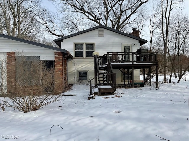 snow covered rear of property with a garage, a chimney, stairway, and a deck