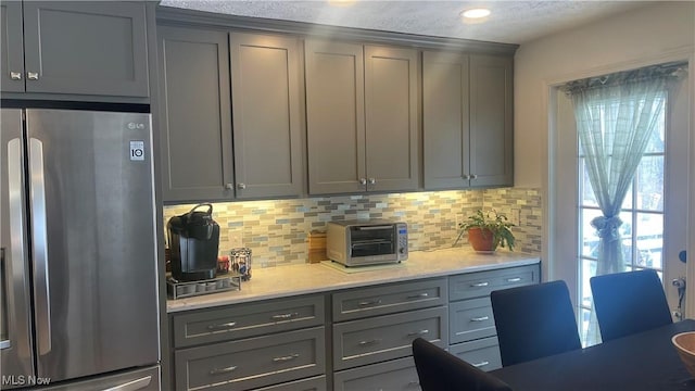 kitchen featuring stainless steel fridge, gray cabinets, and decorative backsplash