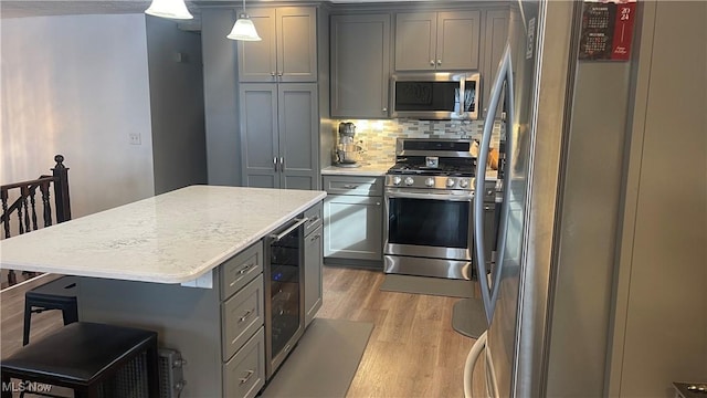 kitchen with light wood-style flooring, beverage cooler, appliances with stainless steel finishes, backsplash, and gray cabinets