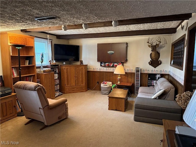 carpeted living room featuring beam ceiling, wainscoting, wood walls, and visible vents