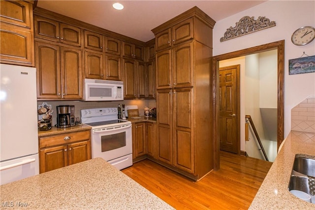 kitchen with light wood-type flooring, light stone counters, and white appliances