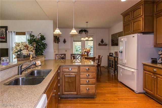 kitchen with pendant lighting, sink, white appliances, light hardwood / wood-style flooring, and light stone countertops