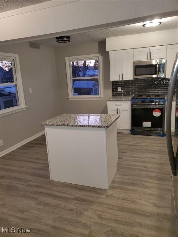 kitchen with white cabinetry, stainless steel appliances, light stone counters, tasteful backsplash, and dark hardwood / wood-style flooring