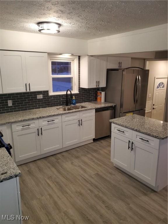 kitchen featuring a sink, wood finished floors, stainless steel appliances, white cabinets, and decorative backsplash