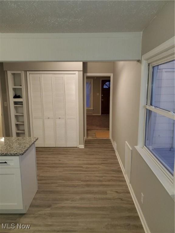 hall with dark wood-type flooring, a textured ceiling, and built in shelves