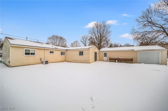 snow covered property with a garage, an outbuilding, and central air condition unit