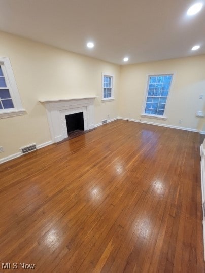 unfurnished living room featuring wood-type flooring and a brick fireplace