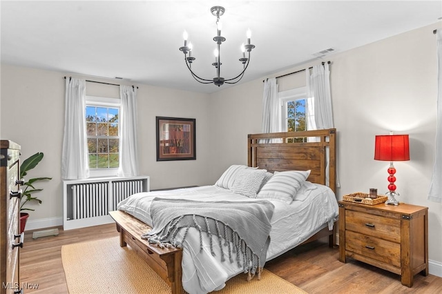 bedroom featuring radiator heating unit, a chandelier, and light wood-type flooring