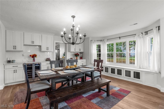 dining space featuring beverage cooler, a chandelier, and light hardwood / wood-style floors