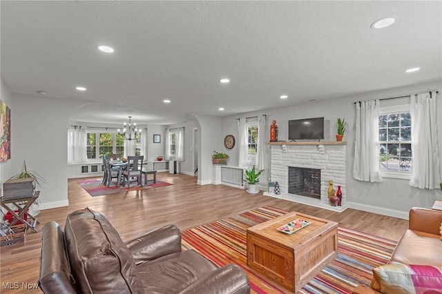 living room with wood-type flooring, a stone fireplace, and an inviting chandelier