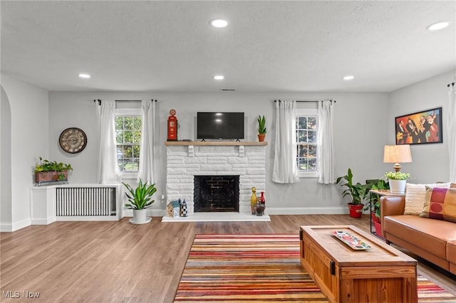 living room with wood-type flooring, a fireplace, radiator, and a textured ceiling