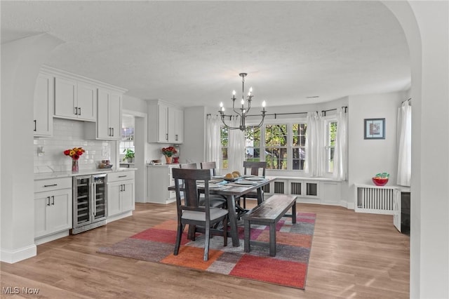 dining room featuring radiator heating unit, beverage cooler, a chandelier, and light wood-type flooring