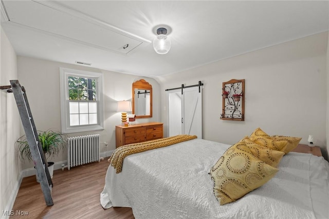 bedroom featuring radiator heating unit, a barn door, and wood-type flooring