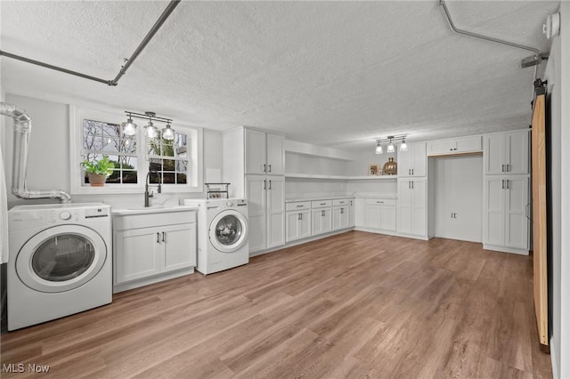 clothes washing area featuring cabinets, sink, a textured ceiling, and light wood-type flooring