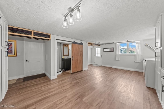 unfurnished bedroom with a barn door, light hardwood / wood-style flooring, and a textured ceiling