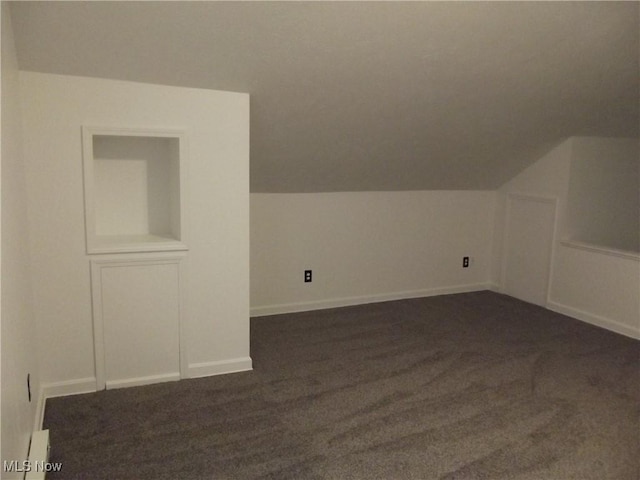 additional living space with dark carpet and vaulted ceiling