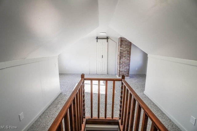 stairs with lofted ceiling, a barn door, and carpet flooring