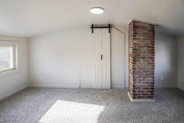 interior space with carpet floors, a barn door, and vaulted ceiling