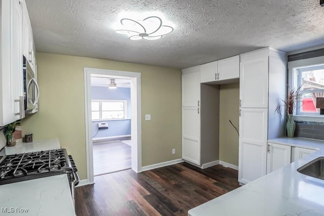 kitchen featuring dark wood-type flooring, white gas stove, a textured ceiling, and white cabinets