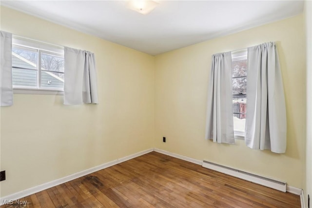 spare room featuring a baseboard heating unit and hardwood / wood-style flooring