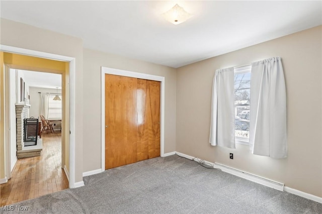 unfurnished bedroom featuring baseboard heating, a fireplace, carpet flooring, and a closet