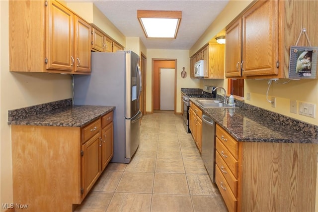 kitchen with sink, a textured ceiling, light tile patterned floors, dark stone counters, and stainless steel appliances