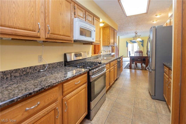 kitchen featuring sink, light tile patterned floors, stainless steel appliances, a textured ceiling, and dark stone counters