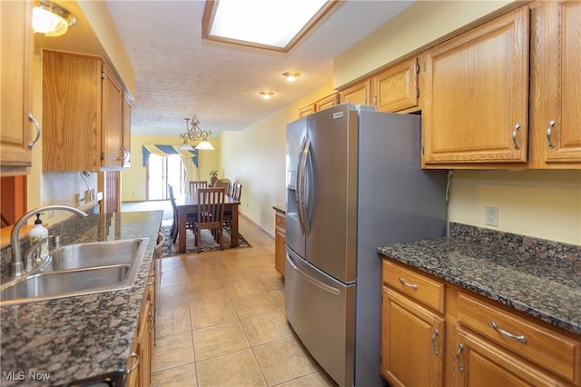 kitchen with sink, stainless steel fridge, a textured ceiling, light tile patterned flooring, and dark stone counters