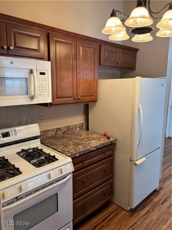 kitchen featuring pendant lighting, dark stone countertops, white appliances, dark wood-type flooring, and an inviting chandelier