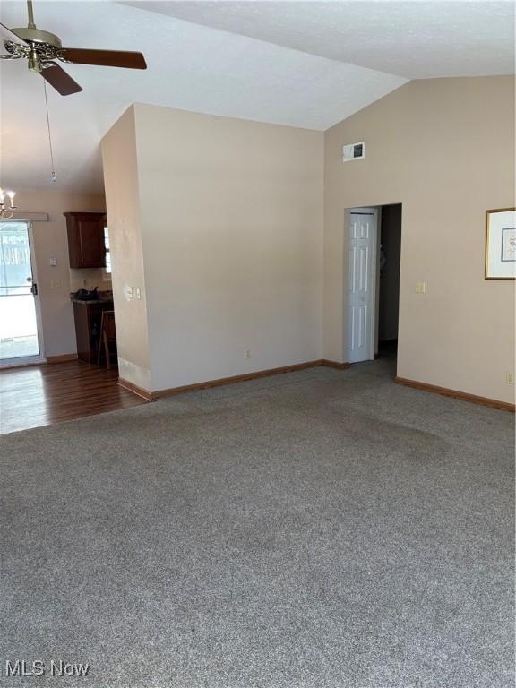 empty room featuring ceiling fan with notable chandelier, carpet flooring, and vaulted ceiling