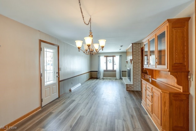 unfurnished dining area featuring an inviting chandelier, a fireplace, and light hardwood / wood-style flooring