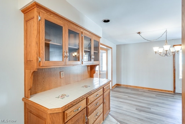 kitchen with tile countertops, a notable chandelier, light hardwood / wood-style floors, and decorative light fixtures