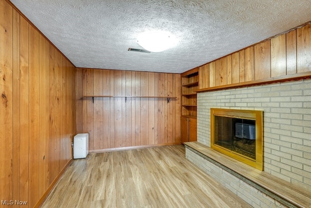 unfurnished living room featuring light hardwood / wood-style flooring, a fireplace, built in shelves, and wooden walls