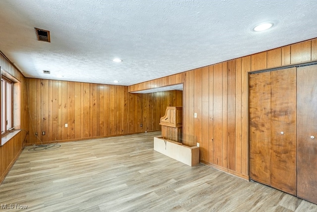 unfurnished living room with light wood-type flooring, a textured ceiling, and wood walls