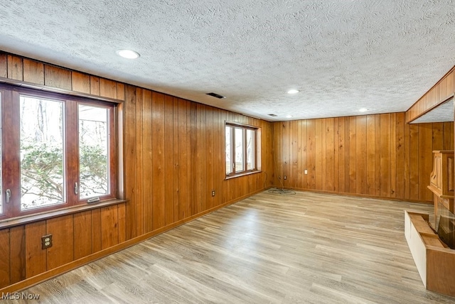 empty room featuring wooden walls, light hardwood / wood-style floors, and a textured ceiling