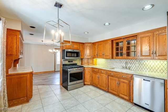 kitchen featuring sink, appliances with stainless steel finishes, backsplash, a notable chandelier, and decorative light fixtures