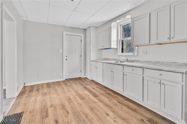 kitchen with sink, a paneled ceiling, white cabinets, and light hardwood / wood-style flooring