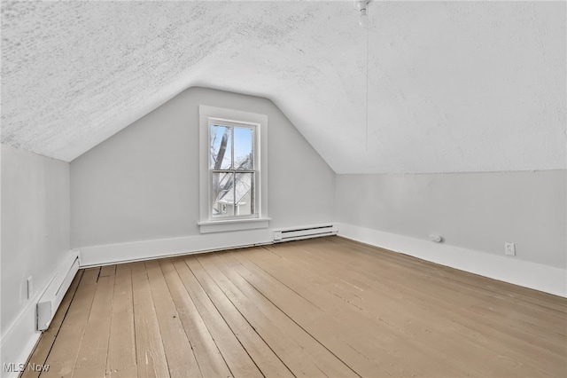 additional living space with vaulted ceiling, a textured ceiling, and a baseboard heating unit