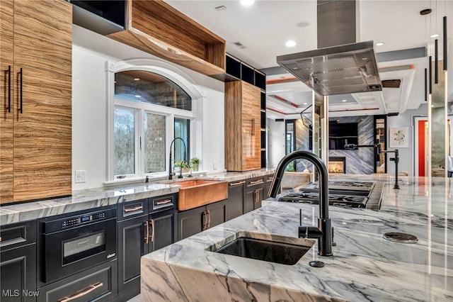 kitchen featuring light stone counters, sink, hanging light fixtures, and island exhaust hood